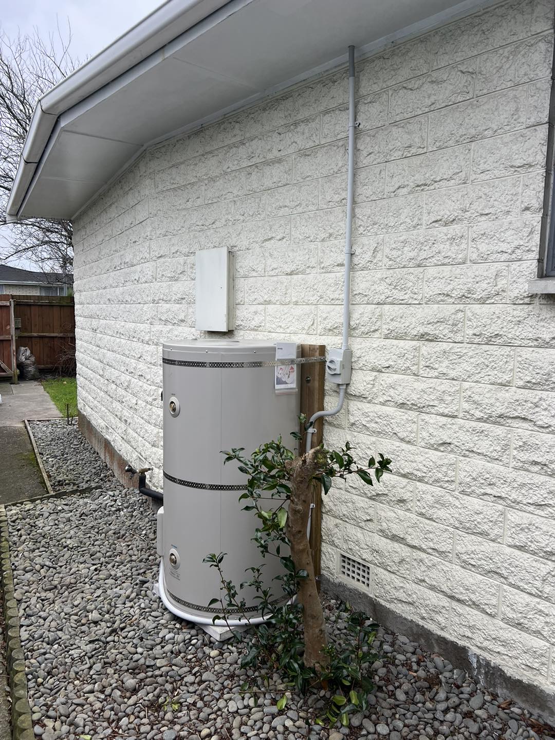 Outdoor white cylinder against a textured white brick wall in a cottage garden, Christchurch