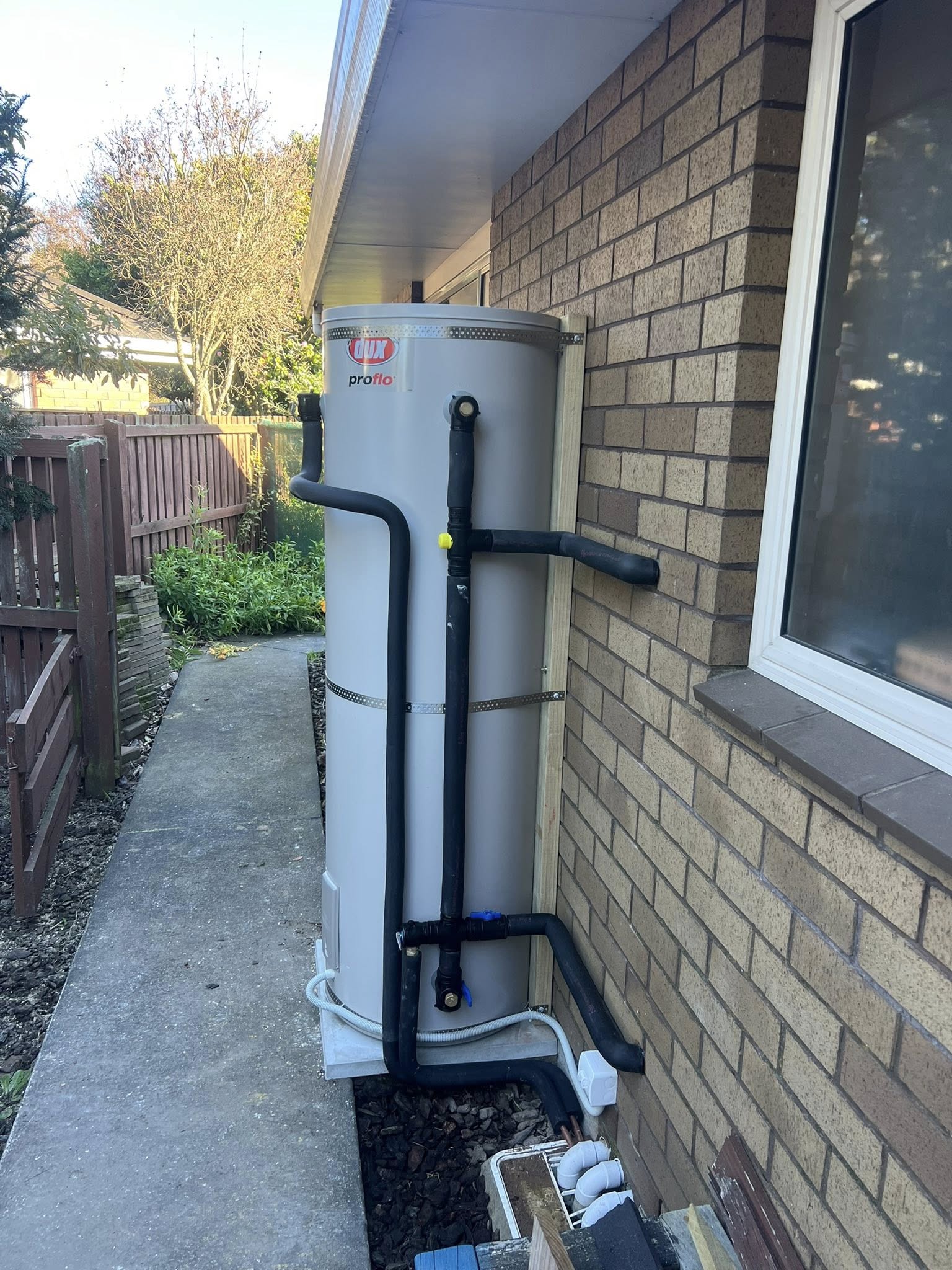 Proflo outdoor cylinder installed against a brown brick wall with neat black pipework