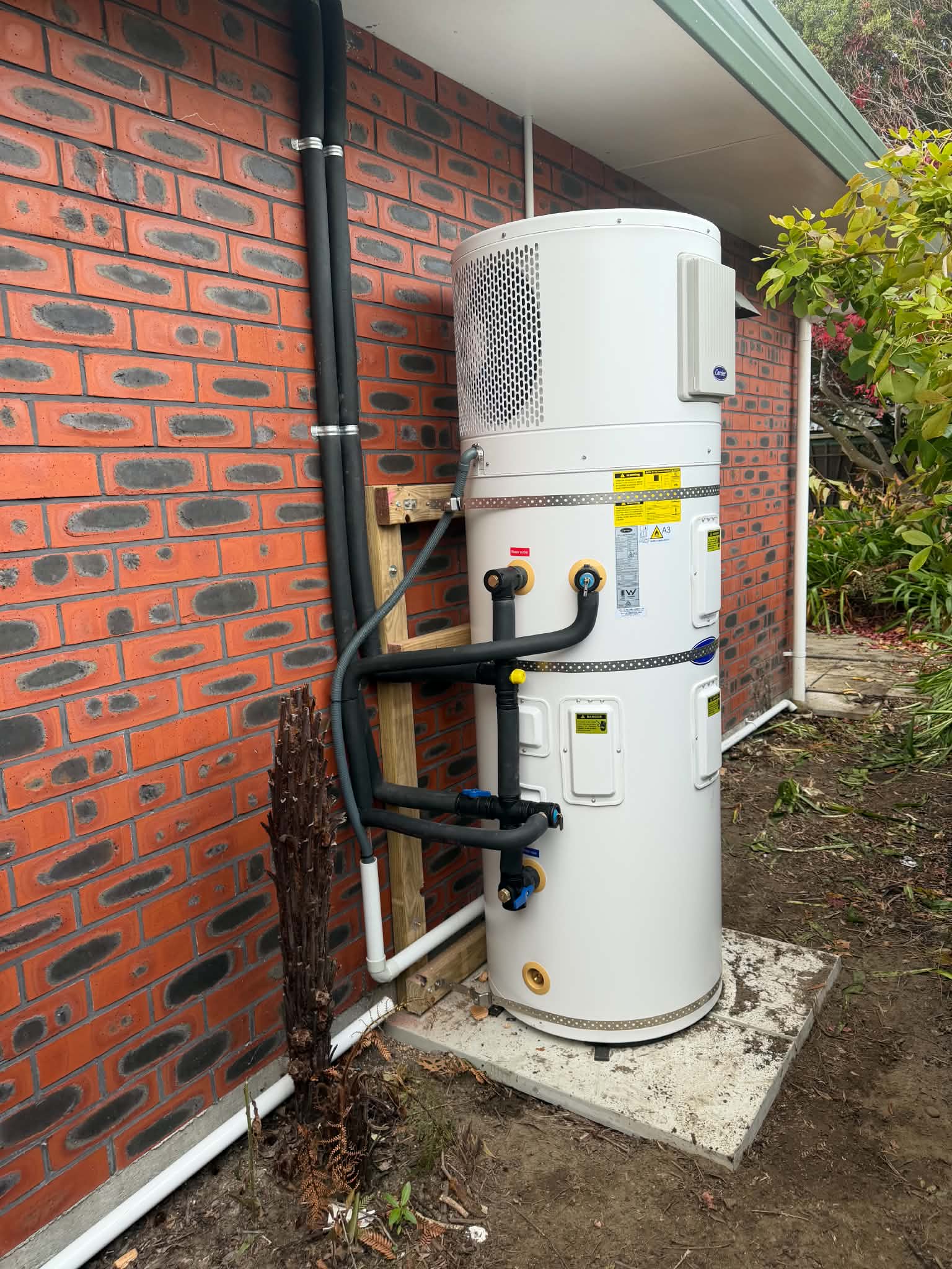 Carrier heat pump hot water unit installed against a red brick wall
