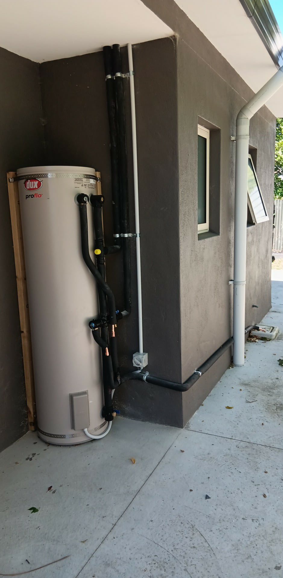 Dux Proflo cylinder mounted outdoors with full pipework run along a stucco corner